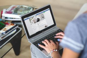 caucasian hands typing on a laptop keyboard with Facebook pulled up.