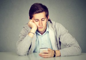 young caucasian man looking at his phone with one hand on his cheek