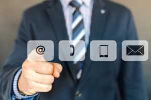 torso of a man in a suit pointing at an email button which is next to a phone button, tablet button and mail button.
