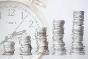 coins stacked going upwards and a clock in the background