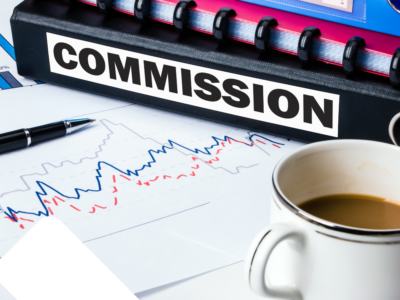 A binder labeled "Commission" placed on a desk, accompanied by a cup of coffee, a pen, and a chart highlighting financial trends.