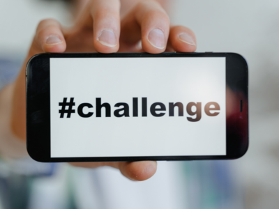 A person holding a smartphone displaying the word "#challenge" on the screen.