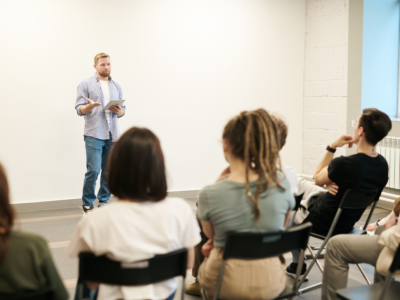 A man giving a presentation to a small group of adults seated in a classroom, symbolizing education and professional licensing.