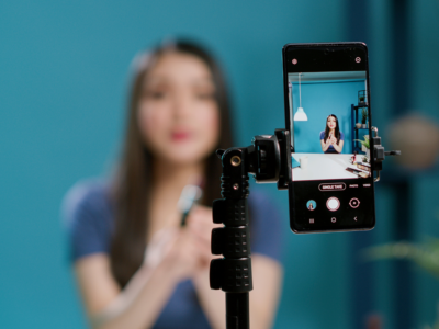 A woman recording a video on her smartphone, which is mounted on a tripod, in a well-lit studio.